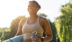 Woman with yoga mat smiling while walking outside