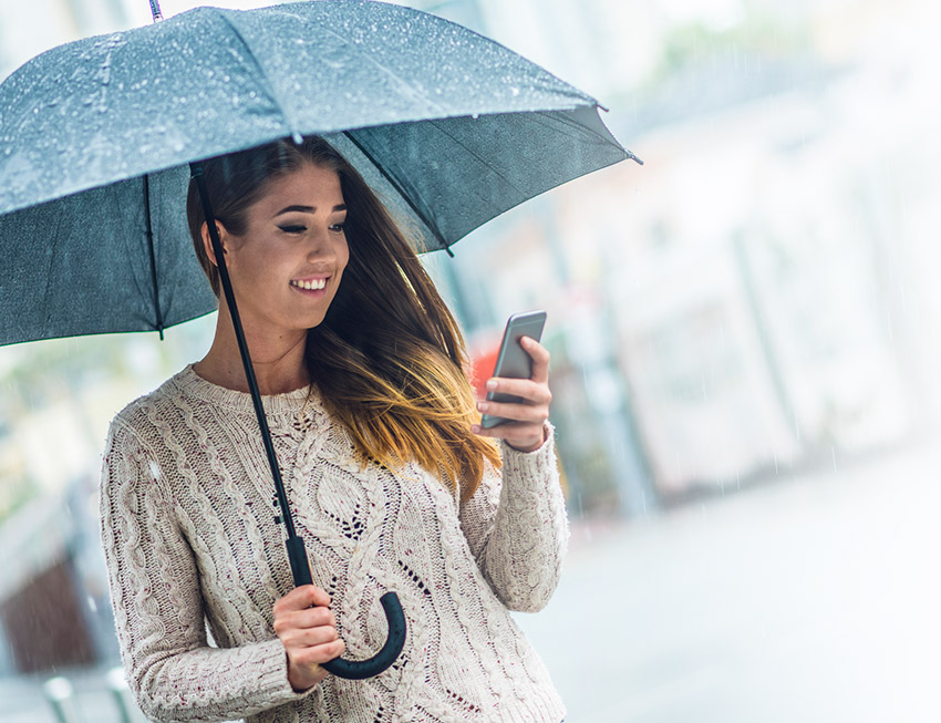 Lady holding umbrella and phone in rain smiling