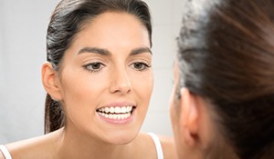 Woman examining her straight teeth in mirror